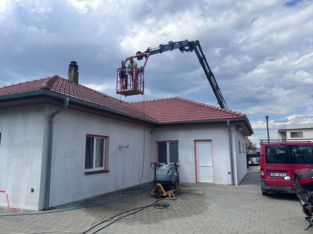 Pracovník na plošině čistí střešní krytinu rodinného domu